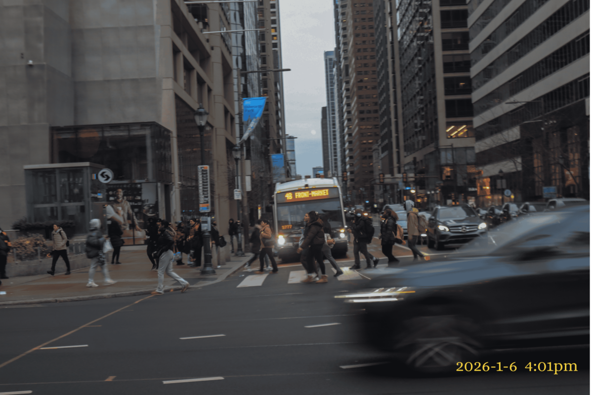 On JFK Boulevard in Philadelphia at 4:01 pm. People are walking across the street as a bus stops.